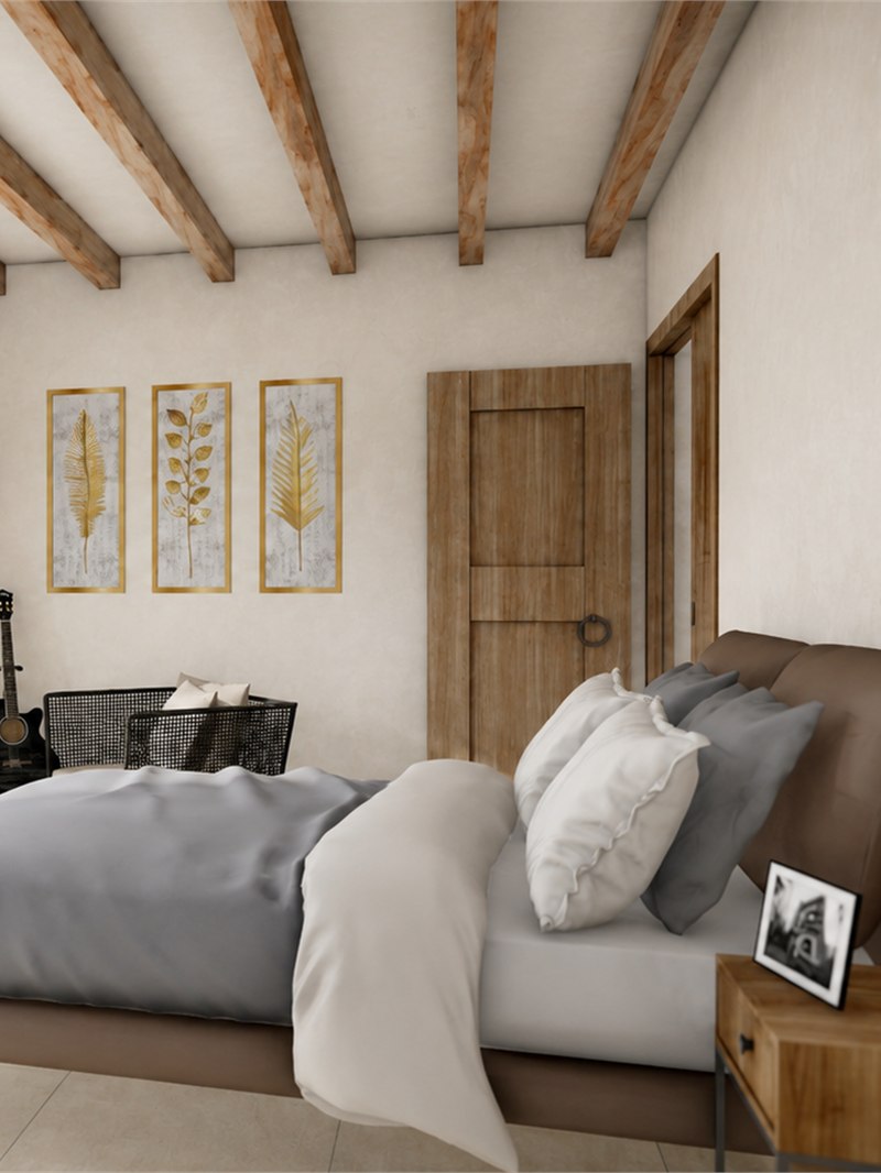 Dormitorio bajo vigas de madera vista, con tres láminas enmarcadas sobre el cabecero y puerta de madera maciza al pasillo